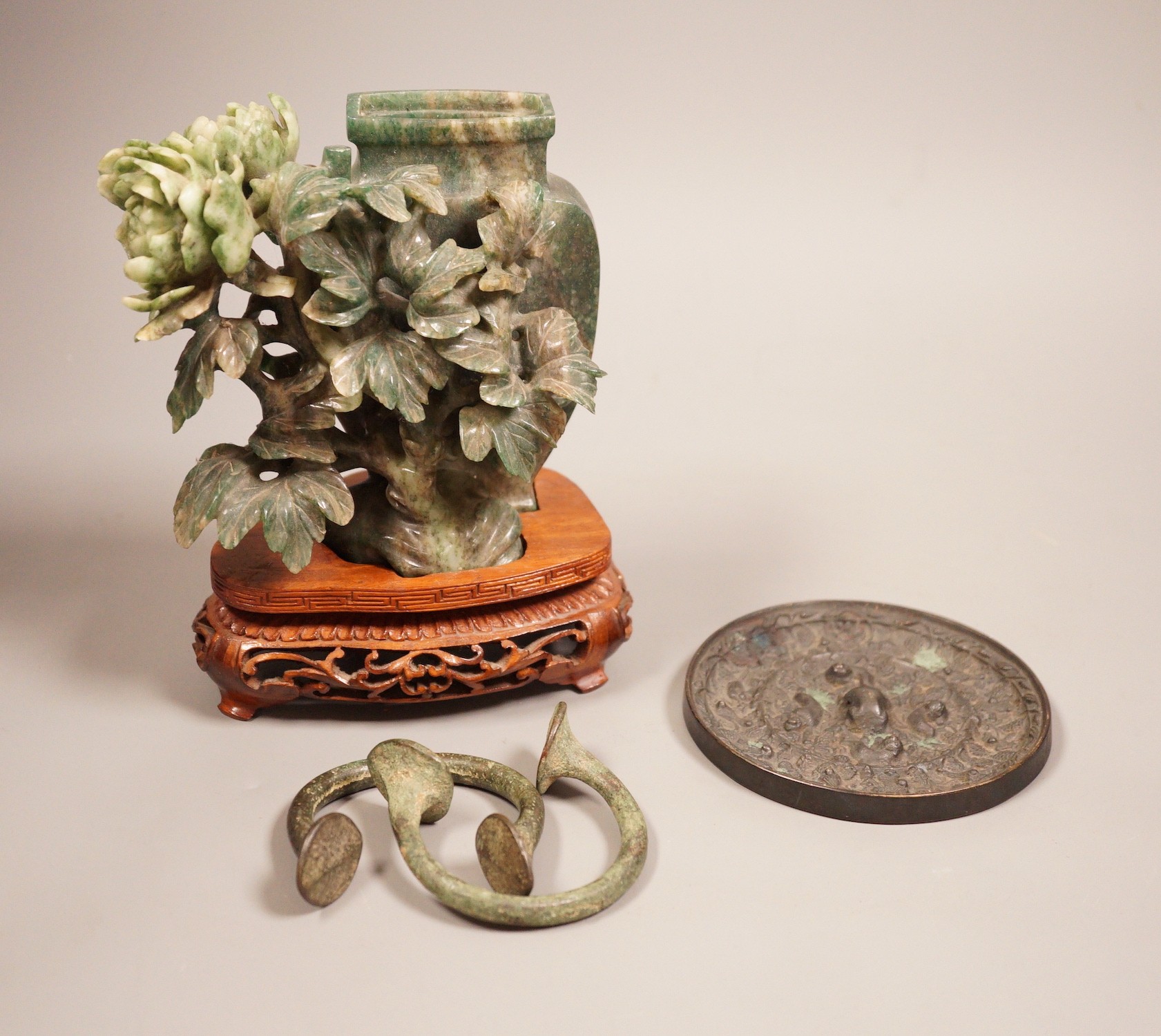 A Chinese bronze mirror, 11cm diameter, a jadeite floral carving on stand with a metal relief plaque, and a pair of bracelets